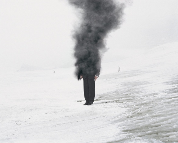 Photography by Andrea Galvani of a man standing in snow with upper half consumed by grey smoke. 