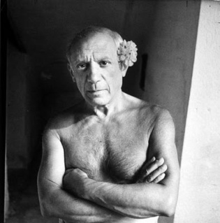 Pablo Picasso shirtless, with flower behind ear.