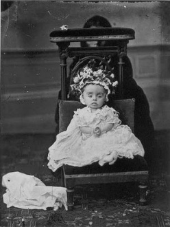 Post mortem photograph of child on chair with hidden mother behind.
