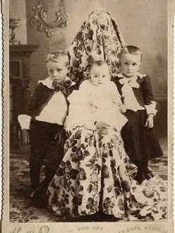 Victorian photograph of three children with mother hidden under draped fabric.